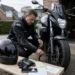 Motorrijder controleert op een Nederlandse oprit de technische staat van zijn motor, met helm, handschoenen en verzekeringspapieren naast zich.